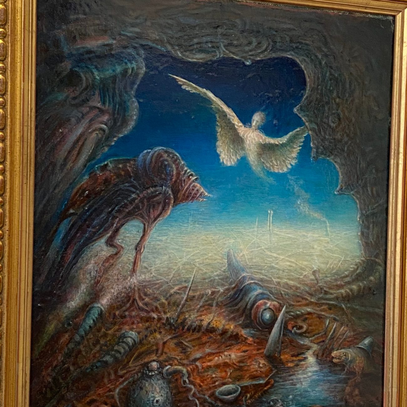 A painting featuring a surrealist scene with a figure resembling an angel in a desolate, hellish landscape with a blue sky.